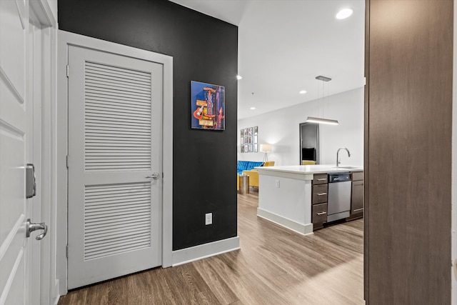 hallway with light wood finished floors, a sink, recessed lighting, and baseboards