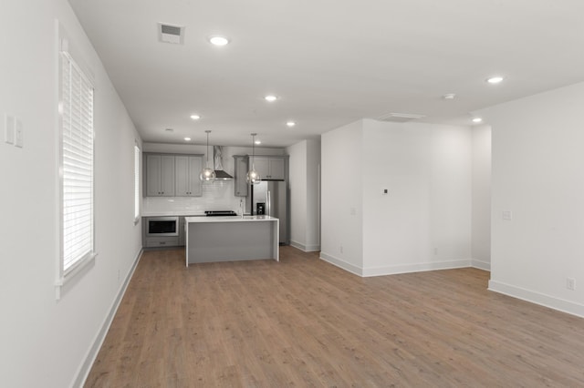 kitchen featuring gray cabinets, stainless steel appliances, recessed lighting, wall chimney range hood, and open floor plan