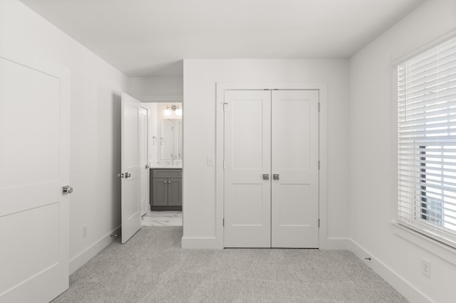 unfurnished bedroom with light carpet, baseboards, a closet, and connected bathroom