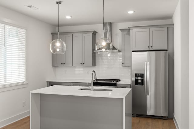 kitchen featuring stainless steel refrigerator with ice dispenser, gray cabinets, wall chimney exhaust hood, a sink, and tasteful backsplash