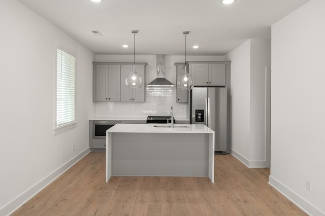 kitchen with wall chimney range hood, stainless steel fridge, gray cabinets, a sink, and recessed lighting
