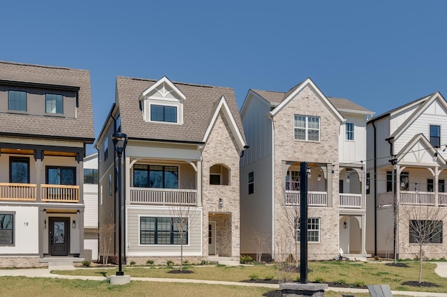 townhome / multi-family property with brick siding, a front yard, and a shingled roof