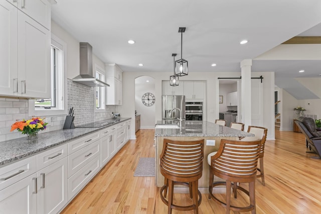 304 Cedar Hollow Ct, Lebanon, TN 37087 - kitchen featuring wall chimney exhaust hood, backsplash, light wood finished floors, stainless steel appliances, and a center island with sink