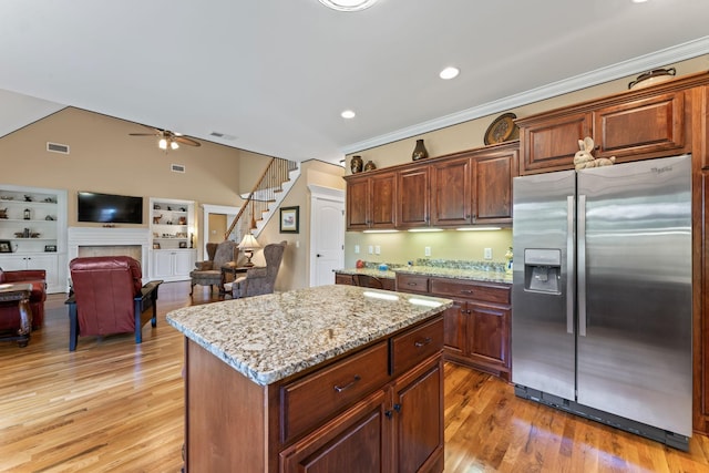 kitchen featuring stainless steel refrigerator with ice dispenser, light stone countertops, a center island, a ceiling fan, and light wood-type flooring