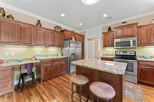 kitchen featuring appliances with stainless steel finishes, light wood-type flooring, a center island, crown molding, and a kitchen breakfast bar