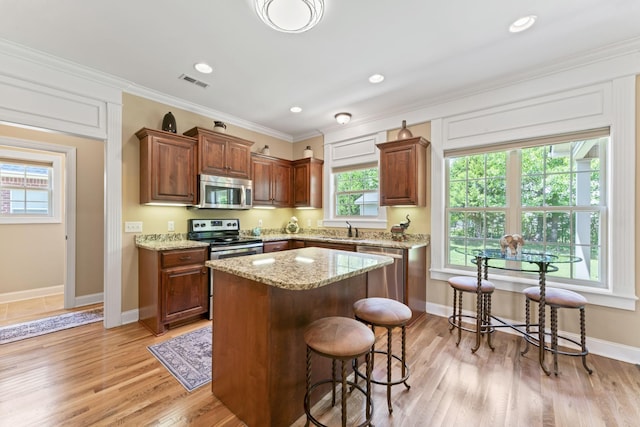 kitchen featuring stainless steel appliances, a sink, a kitchen bar, a center island, and light stone counters