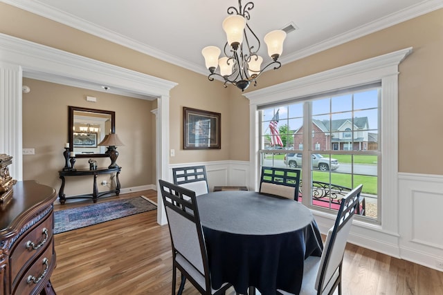 dining room featuring a chandelier, wood finished floors, crown molding, and wainscoting