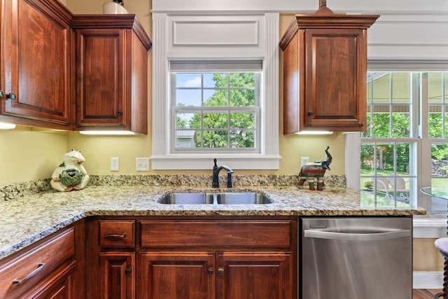 kitchen featuring stainless steel dishwasher, a sink, light stone counters, and healthy amount of natural light