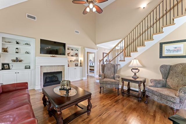 living area featuring ceiling fan, a towering ceiling, stairs, wood finished floors, and a tiled fireplace