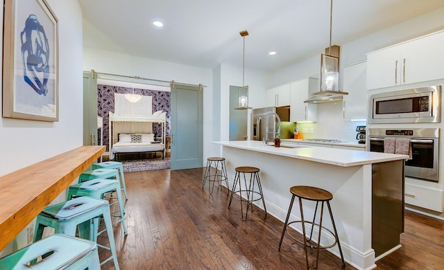 kitchen featuring stainless steel appliances, range hood, a breakfast bar, light countertops, and white cabinetry