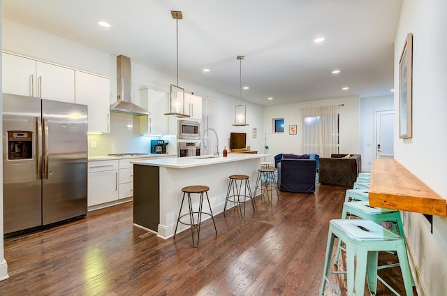 kitchen with stainless steel appliances, wall chimney exhaust hood, a kitchen breakfast bar, open floor plan, and a sink