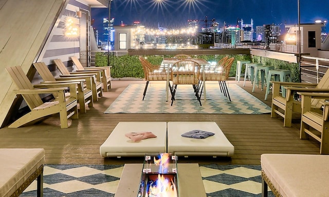 view of wooden balcony with a view of city lights, a deck, exterior bar, and an outdoor fire pit