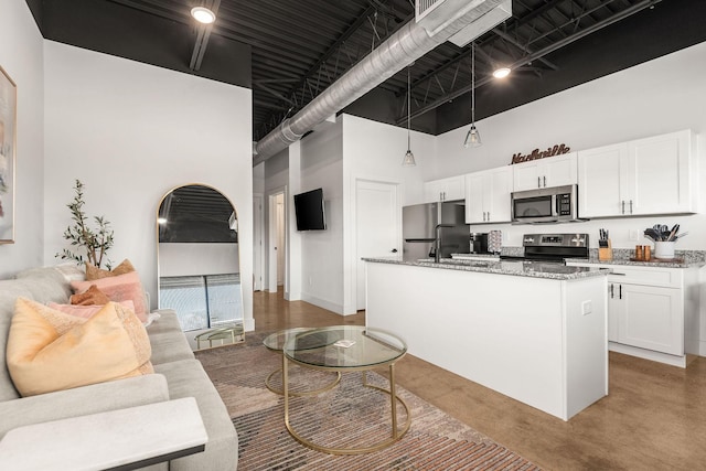 kitchen with stainless steel appliances, a high ceiling, white cabinets, light stone counters, and a kitchen island with sink