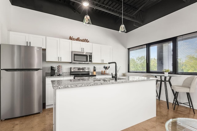 kitchen featuring appliances with stainless steel finishes, a sink, white cabinets, light stone countertops, and a kitchen island with sink