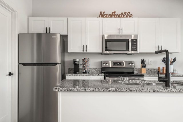 kitchen with appliances with stainless steel finishes, a sink, white cabinets, and stone counters