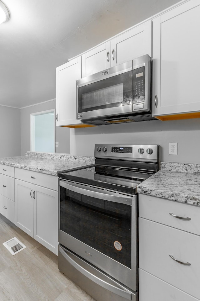 kitchen with stainless steel appliances, light wood-type flooring, white cabinets, light stone counters, and a peninsula