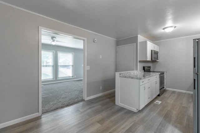 kitchen featuring appliances with stainless steel finishes, wood finished floors, baseboards, white cabinets, and crown molding