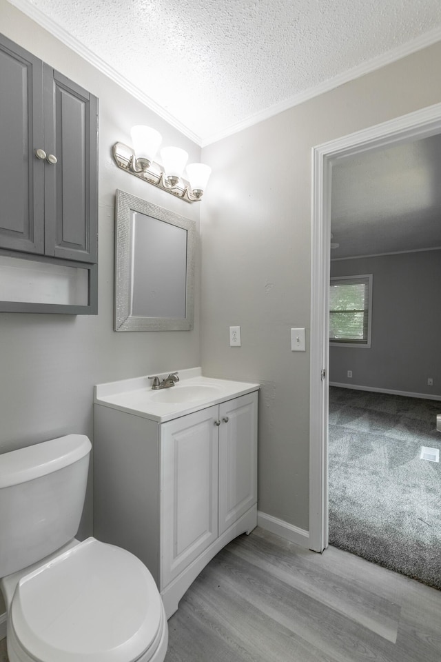 half bath with a textured ceiling, crown molding, toilet, wood finished floors, and vanity