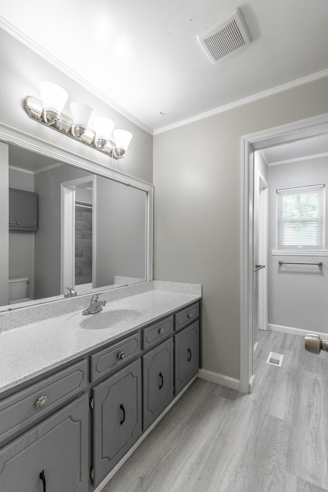 bathroom featuring wood finished floors, vanity, baseboards, crown molding, and toilet
