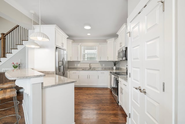 513 Westboro Dr, Nashville, TN 37209 - kitchen with stainless steel appliances, a sink, a peninsula, white cabinetry, and a breakfast bar