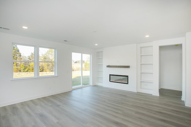 unfurnished living room with wood finished floors, built in shelves, a glass covered fireplace, baseboards, and recessed lighting