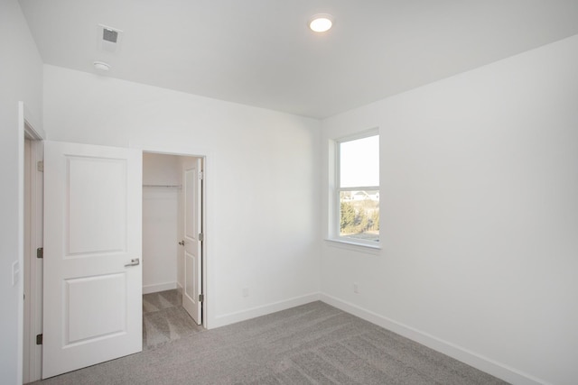 unfurnished bedroom with light carpet, a walk in closet, baseboards, and a closet