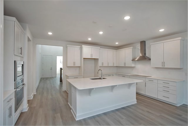 113 W Cassa Way, Mount Juliet, TN 37122 - kitchen with wall chimney range hood, a sink, stainless steel appliances, a center island with sink, and light wood-style flooring