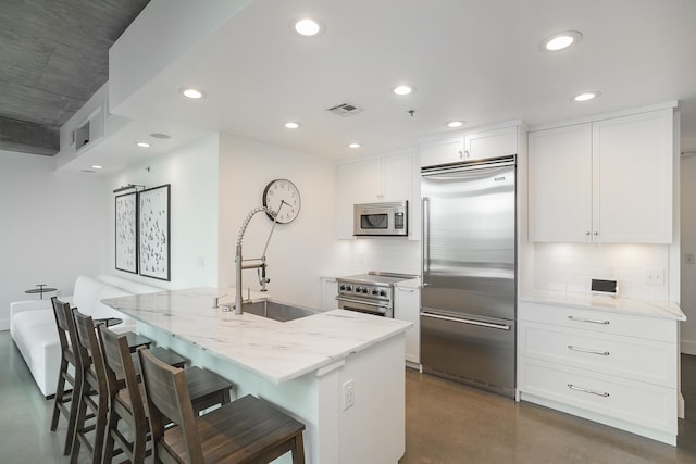 kitchen with premium appliances, a sink, tasteful backsplash, light stone countertops, and recessed lighting