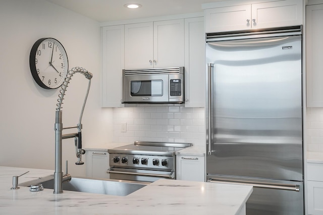 kitchen featuring premium appliances, backsplash, light stone countertops, white cabinets, and recessed lighting