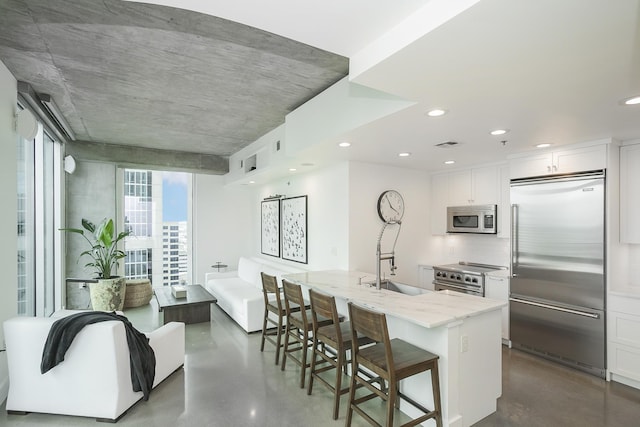 kitchen with stainless steel appliances, concrete flooring, light stone countertops, white cabinetry, and a sink