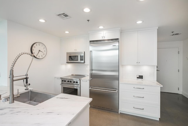 kitchen with high end appliances, a sink, decorative backsplash, recessed lighting, and white cabinetry