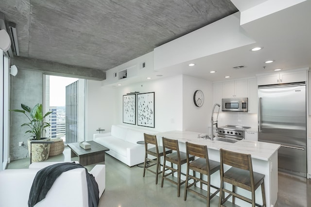 kitchen with appliances with stainless steel finishes, concrete floors, tasteful backsplash, light stone countertops, and a sink