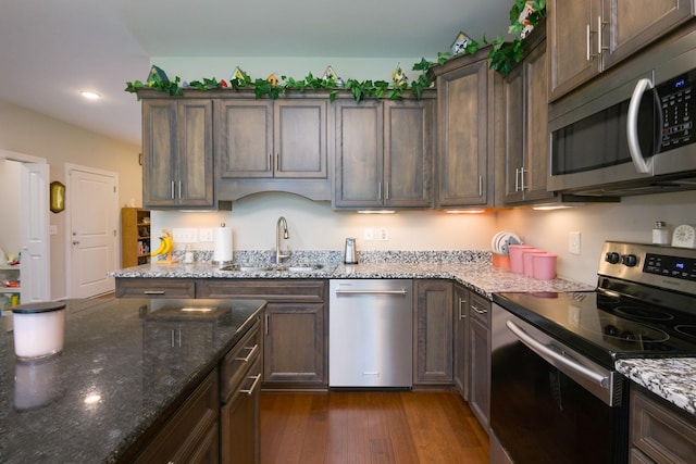 kitchen with stainless steel appliances, a sink, dark stone counters, dark wood-style floors, and recessed lighting