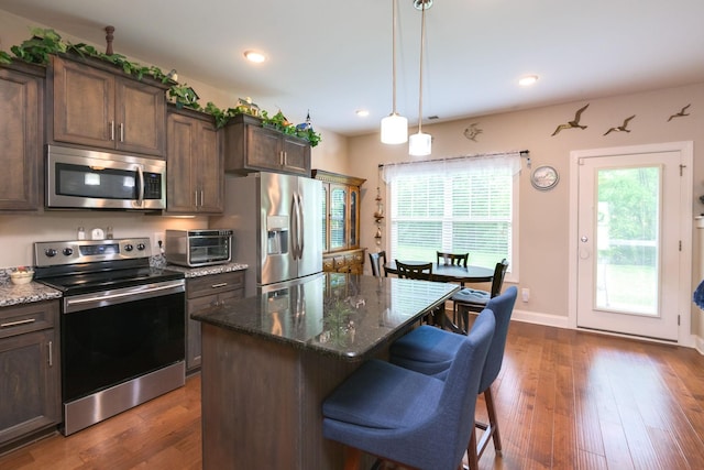 kitchen featuring stainless steel appliances, dark stone countertops, dark brown cabinets, a kitchen bar, and recessed lighting