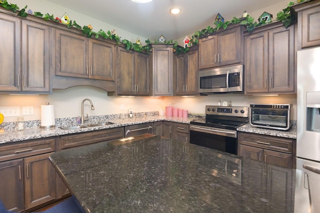 kitchen featuring stainless steel appliances, a sink, stone countertops, recessed lighting, and dark brown cabinets