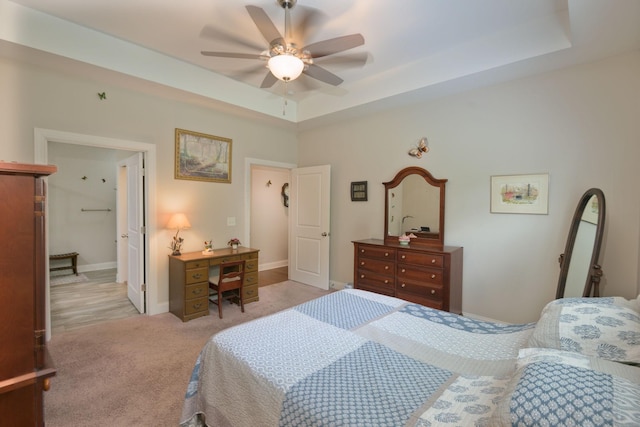 bedroom featuring light colored carpet, a tray ceiling, baseboards, and a ceiling fan