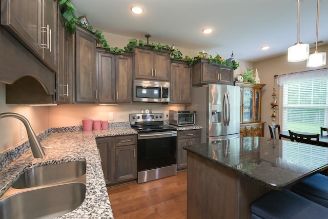 kitchen with appliances with stainless steel finishes, a sink, a breakfast bar area, light wood-style flooring, and light stone counters