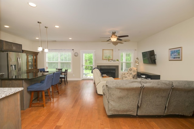 living room featuring light wood-style flooring, a ceiling fan, plenty of natural light, a fireplace, and recessed lighting