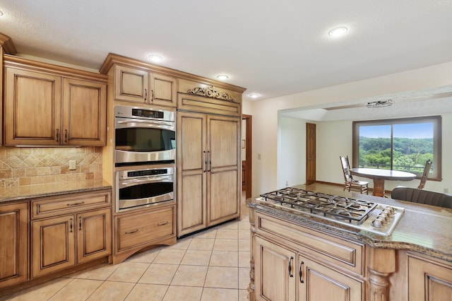1361 Madison Creek Rd, Goodlettsville, TN 37072 - kitchen featuring appliances with stainless steel finishes, light stone counters, light tile patterned floors, brown cabinetry, and recessed lighting