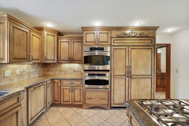 1361 Madison Creek Rd, Goodlettsville, TN 37072 - kitchen featuring stainless steel appliances, decorative backsplash, brown cabinets, light tile patterned floors, and dark stone countertops