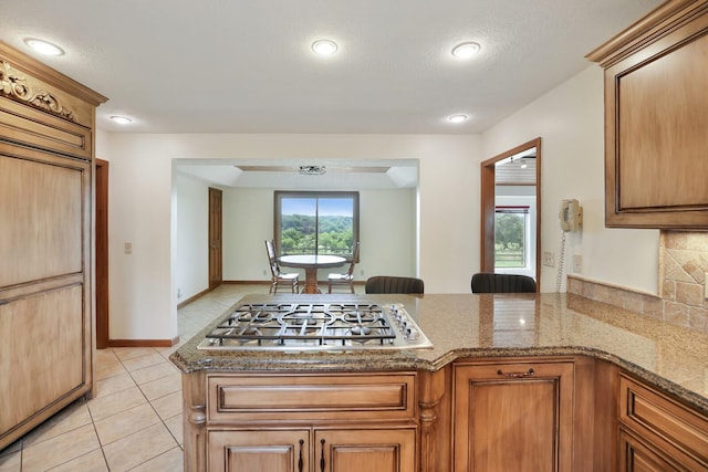 1361 Madison Creek Rd, Goodlettsville, TN 37072 - kitchen featuring stainless steel gas stovetop, a peninsula, light tile patterned floors, stone countertops, and brown cabinetry