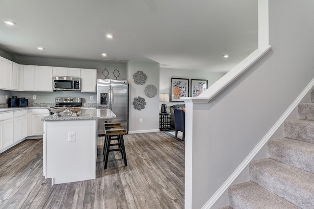 kitchen with appliances with stainless steel finishes, dark wood-style floors, a kitchen island, a kitchen bar, and recessed lighting