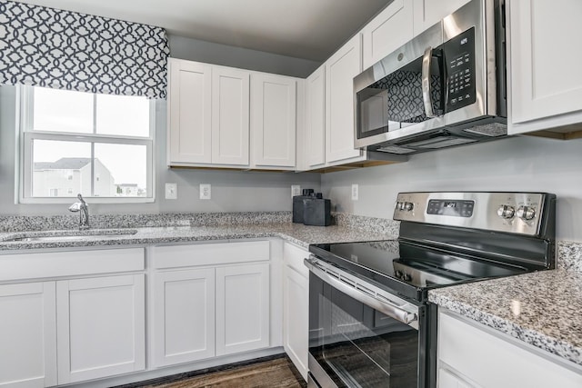 kitchen featuring stainless steel appliances, a sink, white cabinets, and light stone countertops