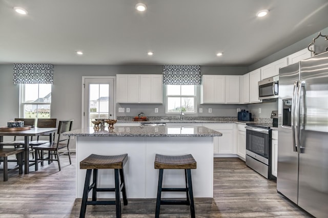 kitchen featuring stainless steel appliances, a sink, a center island, stone countertops, and a breakfast bar area