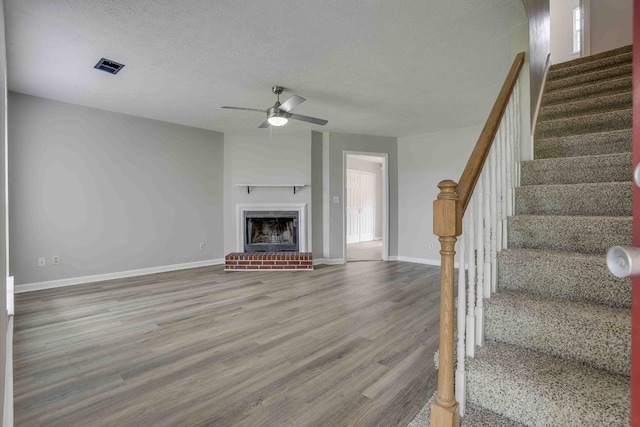 unfurnished living room featuring a ceiling fan, wood finished floors, baseboards, stairs, and a textured ceiling