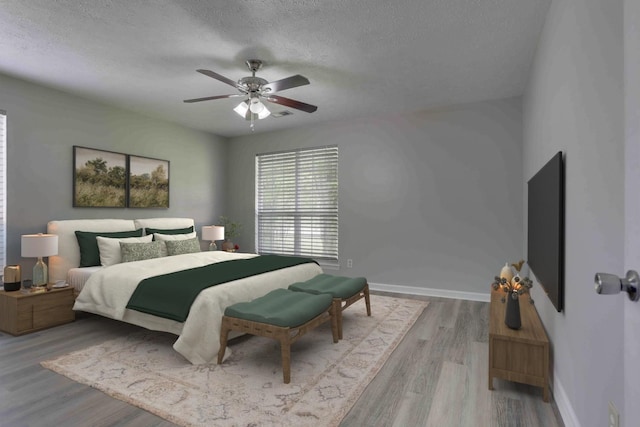 bedroom featuring a textured ceiling, baseboards, wood finished floors, and ceiling fan