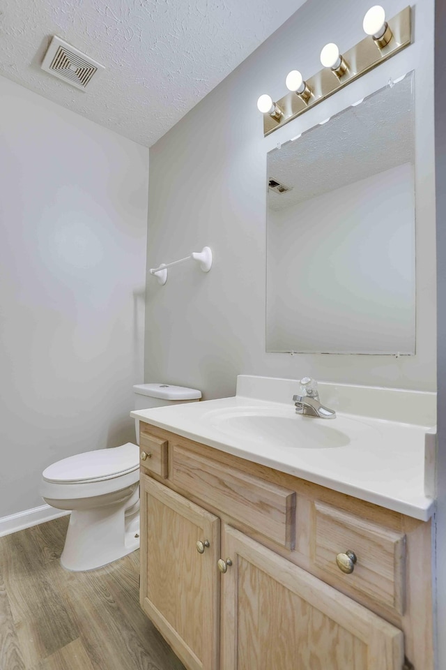 bathroom with wood finished floors, toilet, vanity, and a textured ceiling