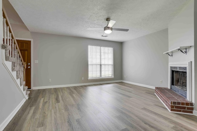 unfurnished living room with stairs, wood finished floors, a ceiling fan, a fireplace, and a textured ceiling