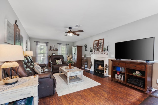 living room with ceiling fan, a warm lit fireplace, and wood finished floors