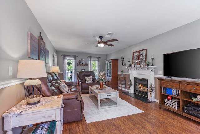 living area featuring a glass covered fireplace, a ceiling fan, and wood finished floors